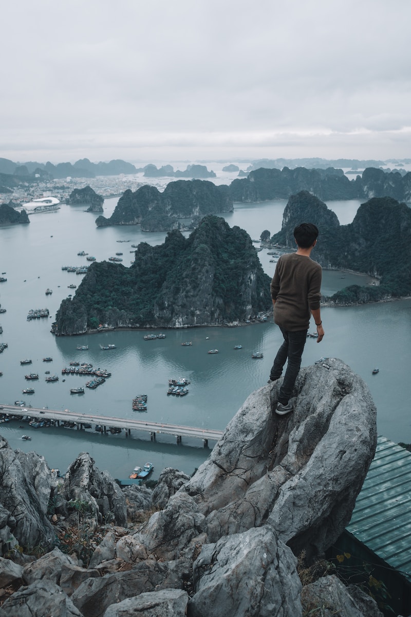 man standing on top of a rocky mountain overlooking ha long bay