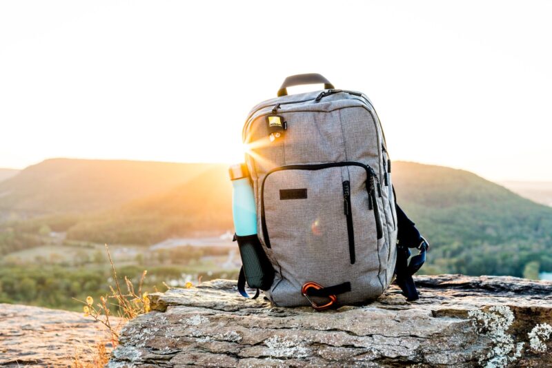 grey and black hiking backpack and cyan tumbler on grey rock during sunset