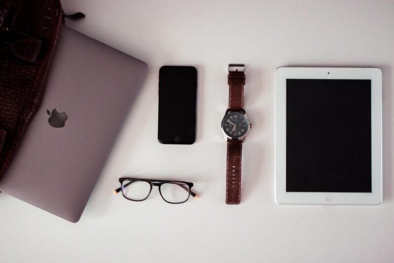 white iPad beside round silver-colored analog watch, black iPhone 5 and black framed eyeglasses on white surface pack for a business trip