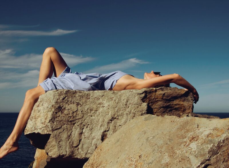 woman in blue denim shorts lying on brown rock during daytime