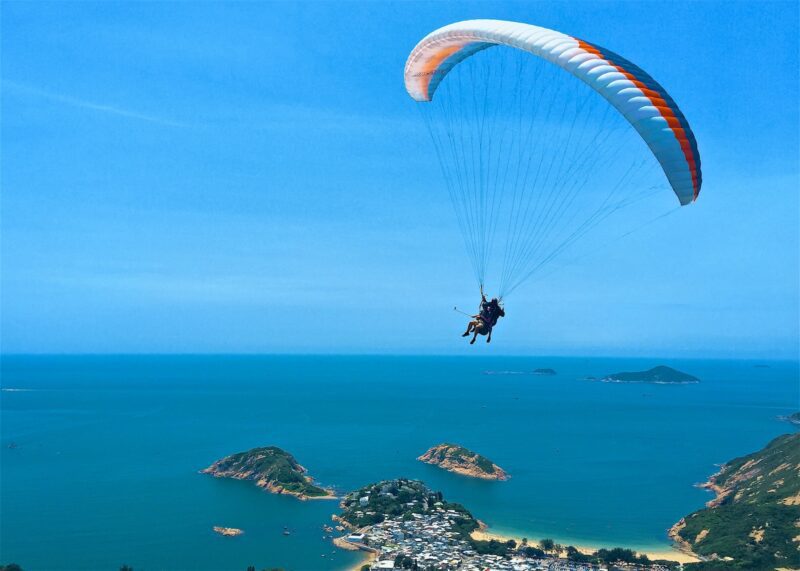 person parachuting over green leaf trees and body of water during daytime