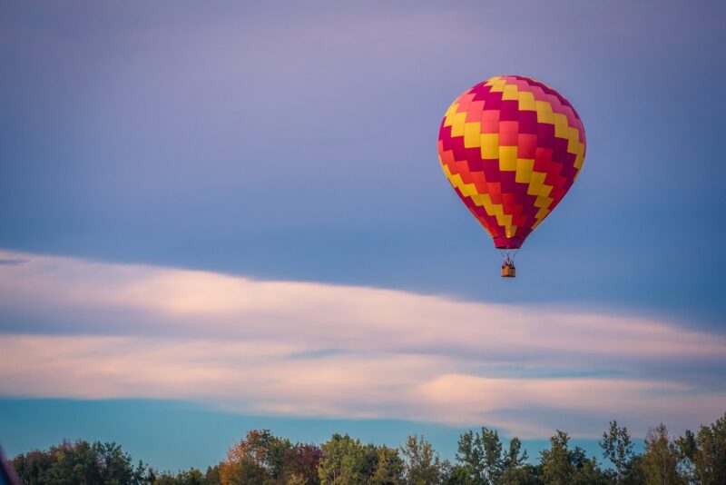 pink and yellow hot air balloon ride over trees