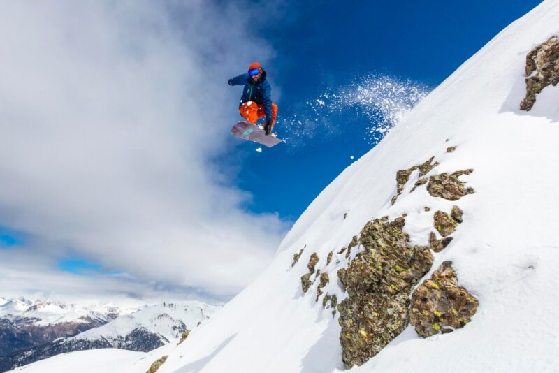 man in red jacket and blue pants sitting on snow covered mountain during daytime