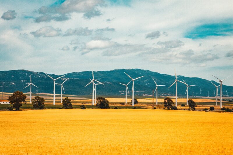 white wind turbines on brown field under blue and white sunny cloudy sky during daytime eco-friendly travel