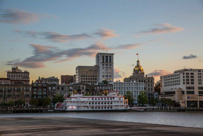 white and brown boat on sea near city buildings during sunset