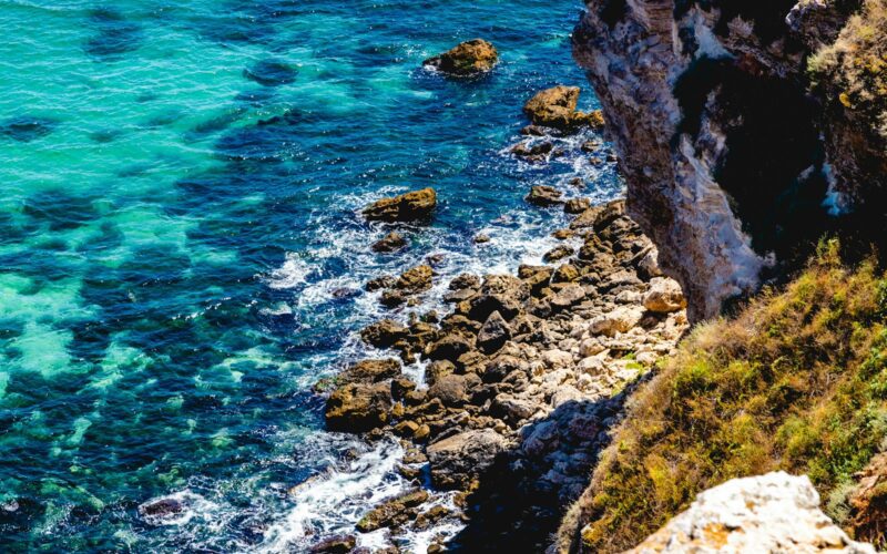 brown rocky mountain beside blue sea during daytime