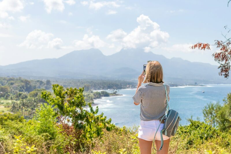 a woman taking a picture of the ocean with her cell phone