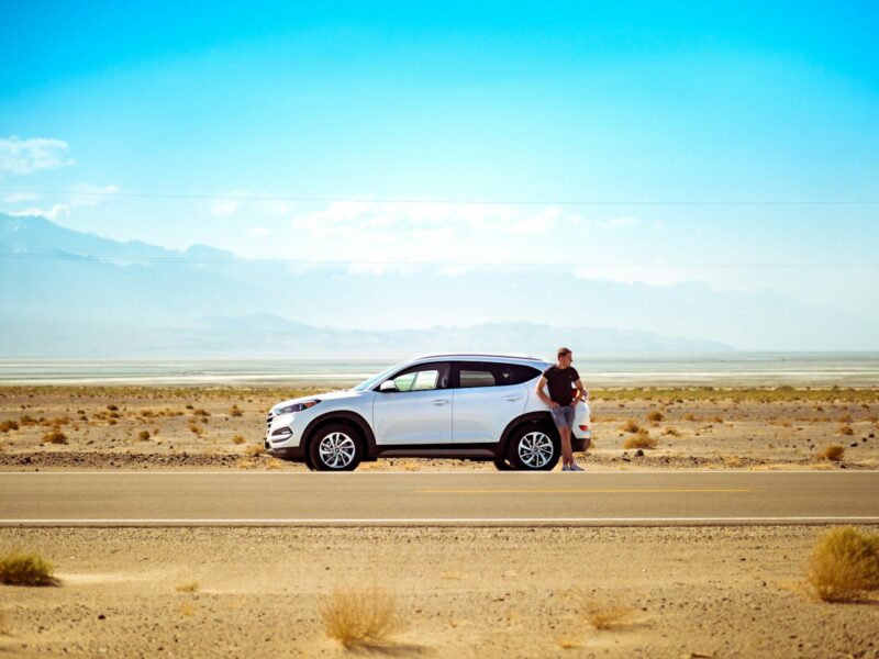 man standing beside white SUV near concrete road under blue sky at daytime